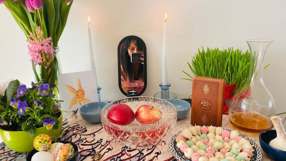 Tisch für «Haft Sin» für das Frühlingsfest im Iran mit Blumen, Äpfel, ein Buch und Kerzen.