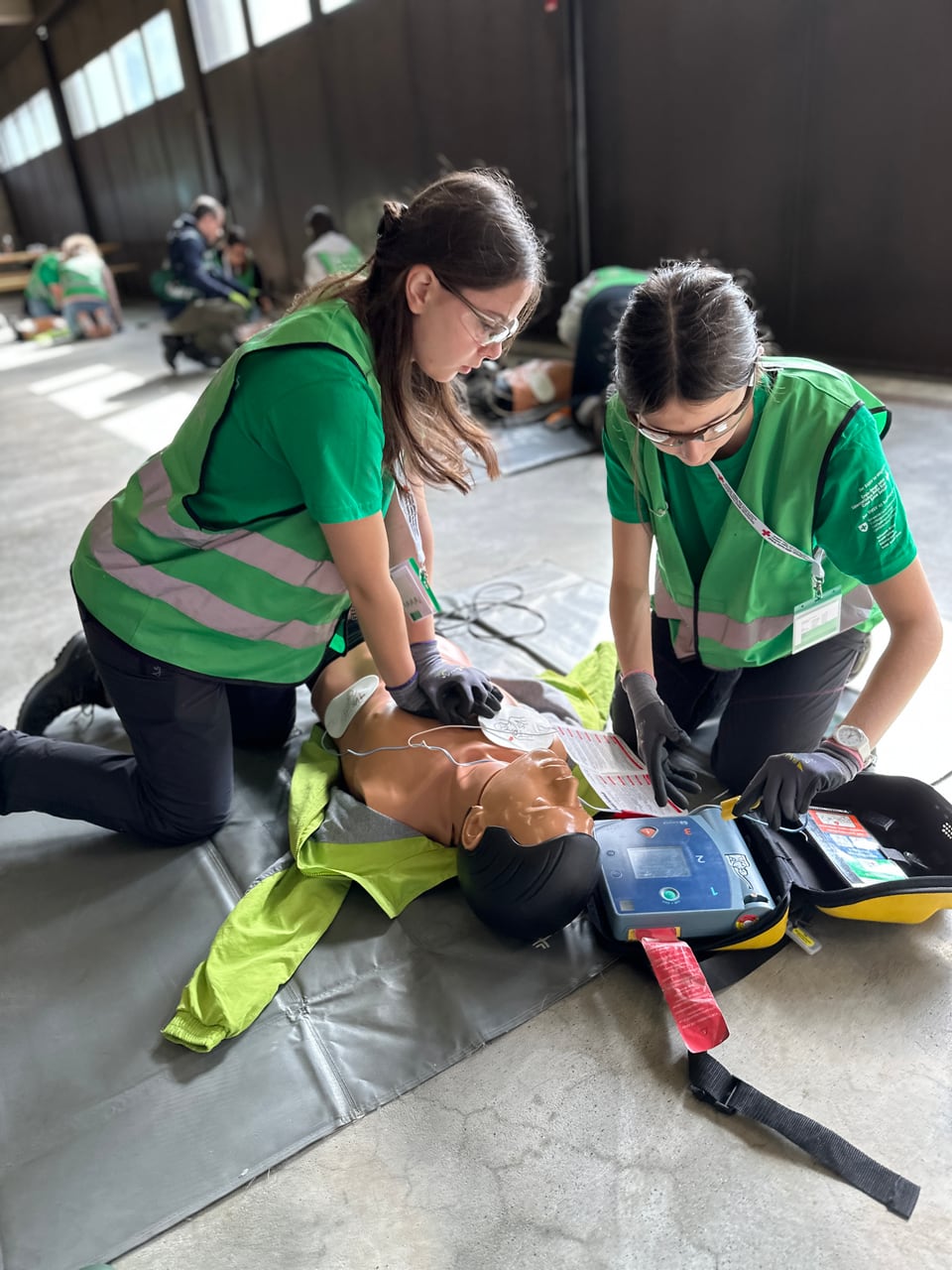 Zwei Schülerinnen üben an einer Reanimationspuppe wie man den AED anwendet.