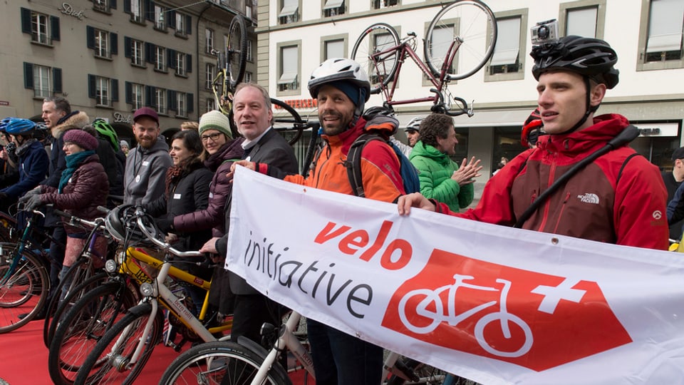 velocipedists en colona che tegnan in placat cun si iniziativa da velo