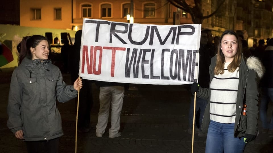 Purtret da la demo dal 2018. Duas dunnas tignan in banner cun scrit si Trump not welcome. 