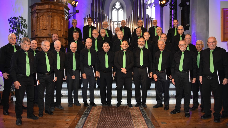 Der Chor viril Domat (Männerchor Domat) steht in einer Kirche, alle in schwarz und mit gründer Krawatte.