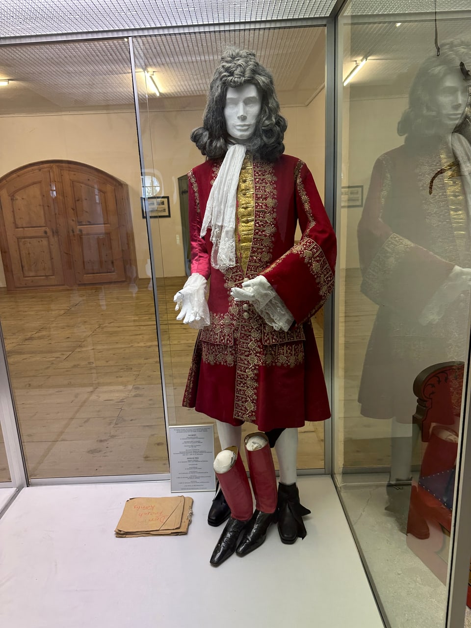 In einer Vitrine steht ein Mannequin mit einem dunkelroten antiken Mantel.