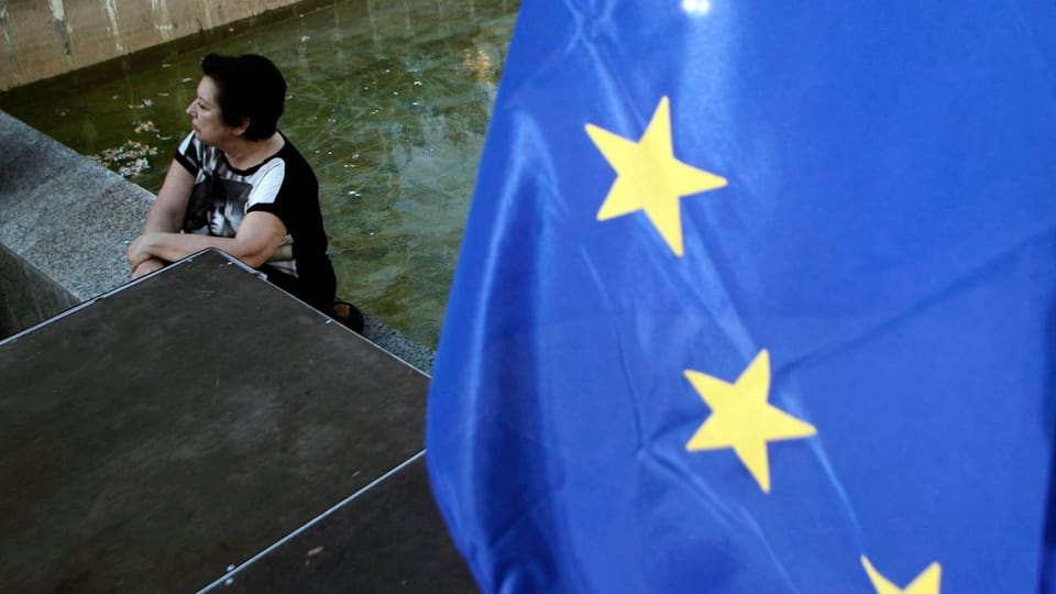 dunna pensiva che sesa, dretg dad ella ina bandiera da l'UE