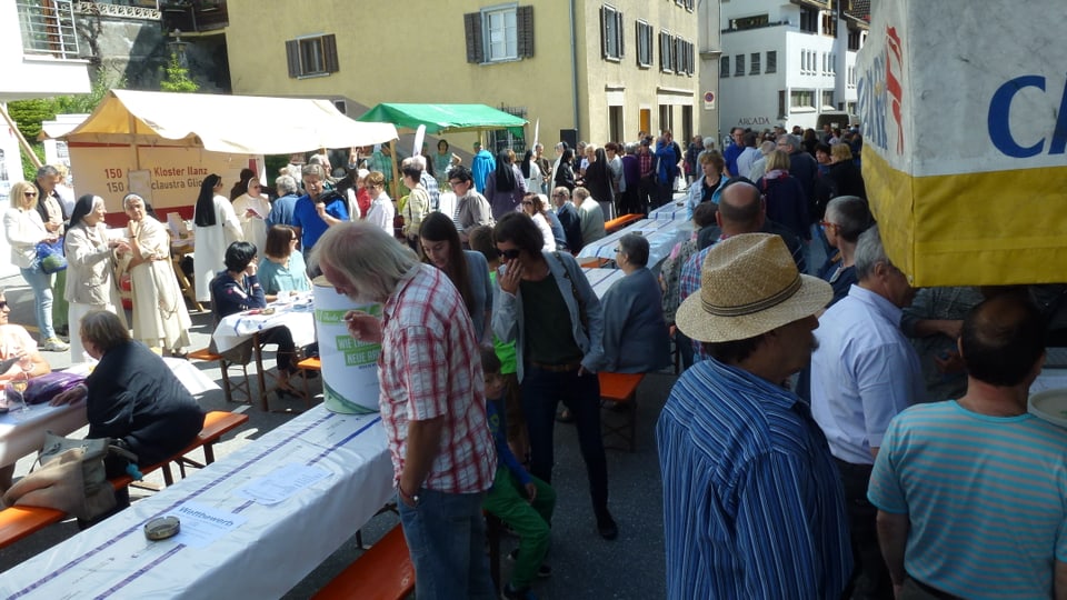 Plazza da festa cun bancs, maisas e blers visitaders.