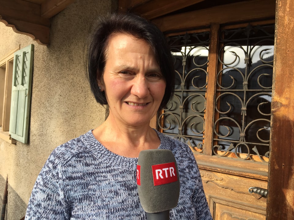 Maria Decurtins tegn il microfon da RTR avan l'isch chasa a Darvella