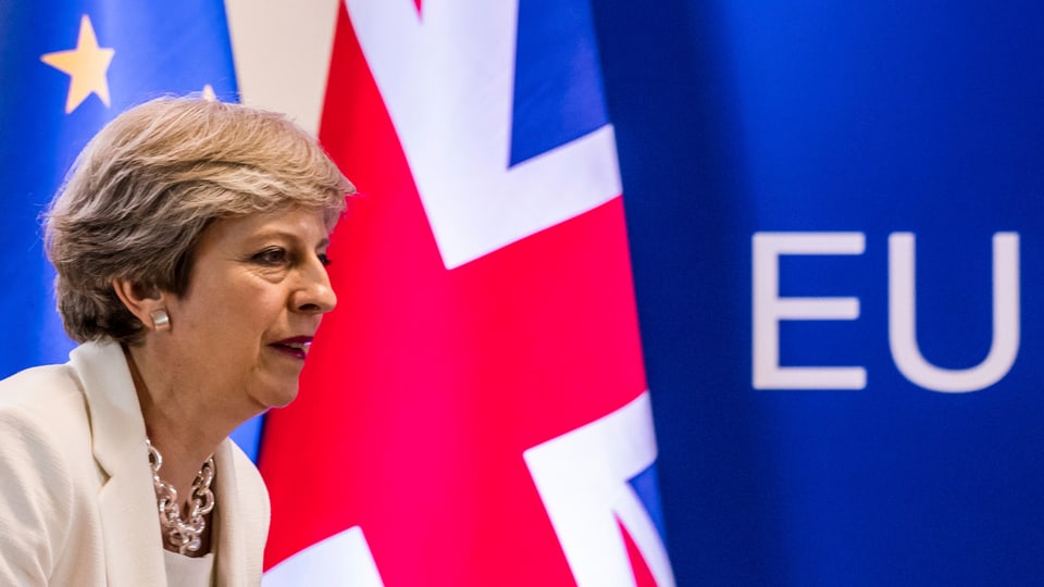 Theresa May avant las bandieras da la Gronda Britannia e da l'UE.