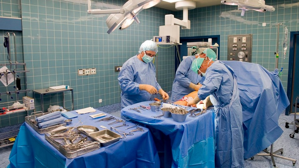 3 medis vid en ina sala d'operaziun vid operar in pazient.