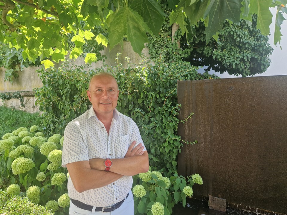 Ein Mann steht vor einer Hecke in einem Garten.
