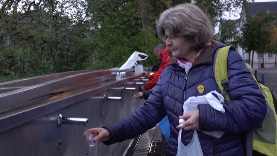 Eine Frau füllt Wasser von Lourdes in eine Flasche.