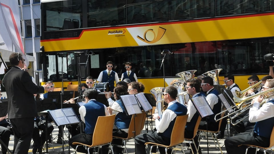 Ils musitcants da la Musica instrumentala Salouf Mon Stierva, che sunan sin sutgas da lenn davant in auto da posta mellen.