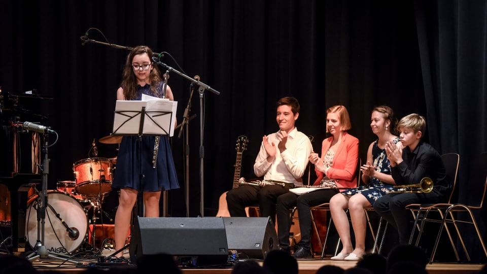 Giuvens e giuvnas musicistas sin ina tribuna.