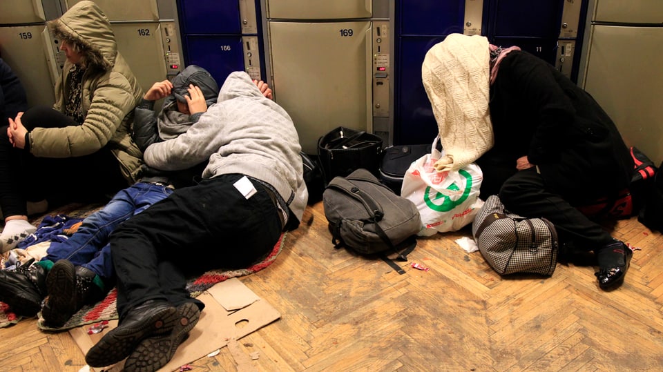 Quatter persunas schain per terra ad ina staziun da tren ed han cuvert il chau cun in lenziel. 