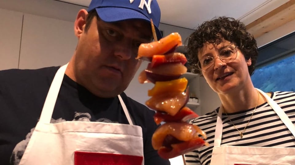 Spidun cun pulaster, peperoni e tschagula Sergio hält den Bratspiess in die Kamera, Simona steht neben ihm.