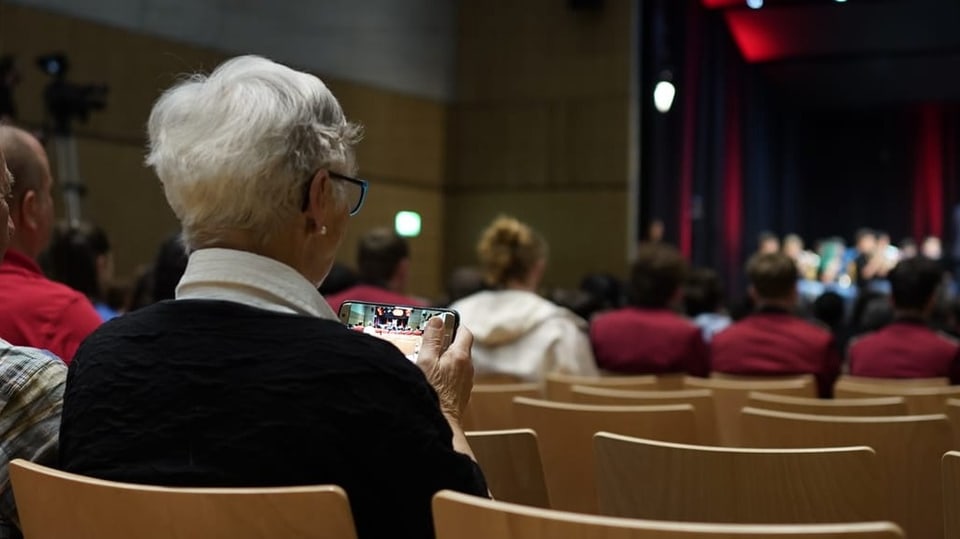 Eine ältere Dame zeichnet das Konzert auf ihrem Handy auf.