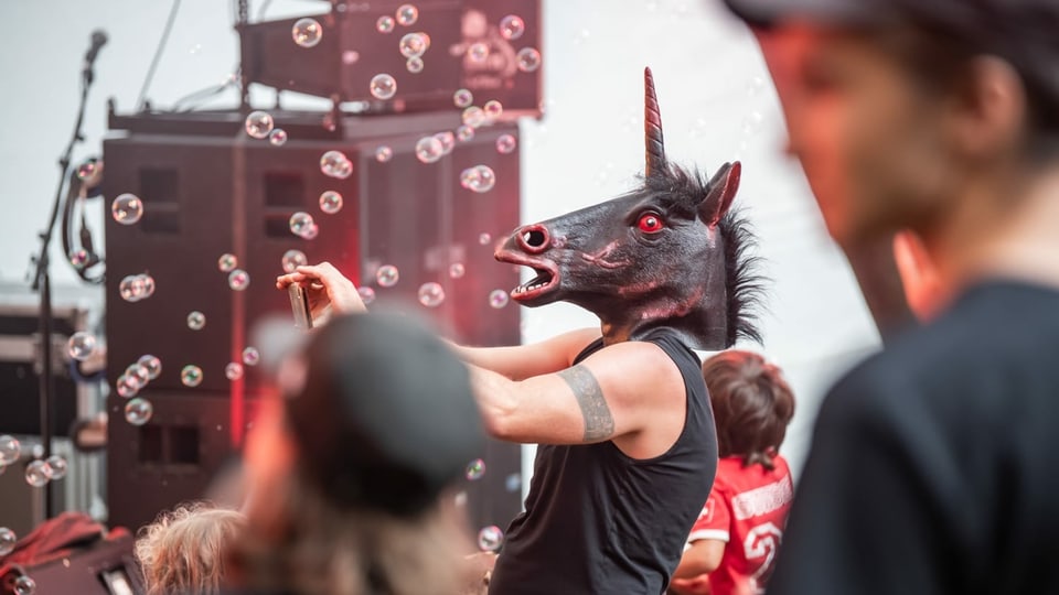 Open Air Stussavgia. Das Einhorn ist beim Auftritt von Okto Vulgaris Pflicht. Der Protagonist unter der Haube ist Simon aus Bad Ragaz. Er tritt ab und zu mit der Sängerin Sarah als Drummer auf und ist nebenbei Groupie der Band.