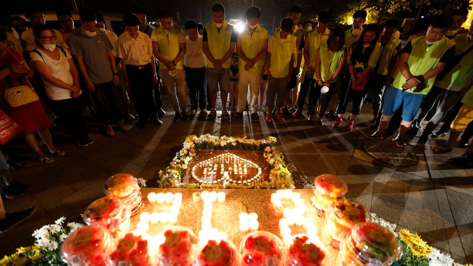 Abitants da Tianjin uran per las unfrendas dals 12 d'avust davant flurs e chandailas.