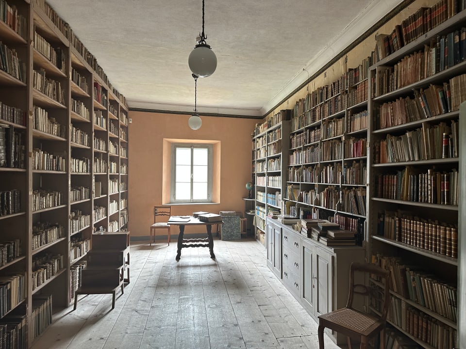 Ein Zimmer, das links und rechts Gestelle voller Bücher hat, vom Boden bis zur Decke.