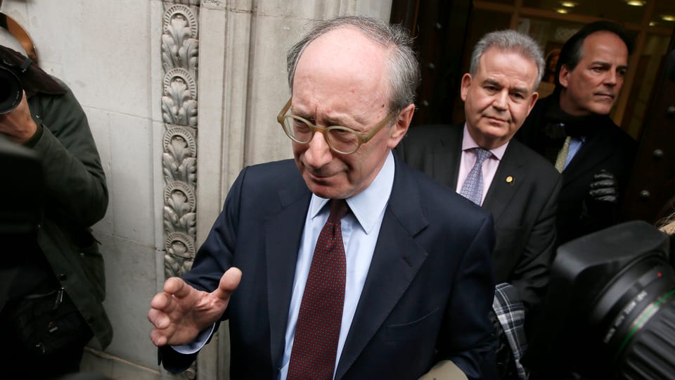 Malcolm Rifkind cun spievel e cravatta circumdà da fotografs. 