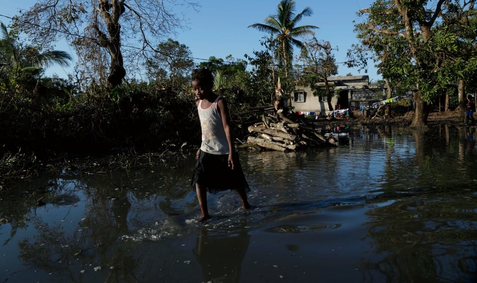 Purtret d'in uffant che passa tras aua che las inundaziuns han purtà. 