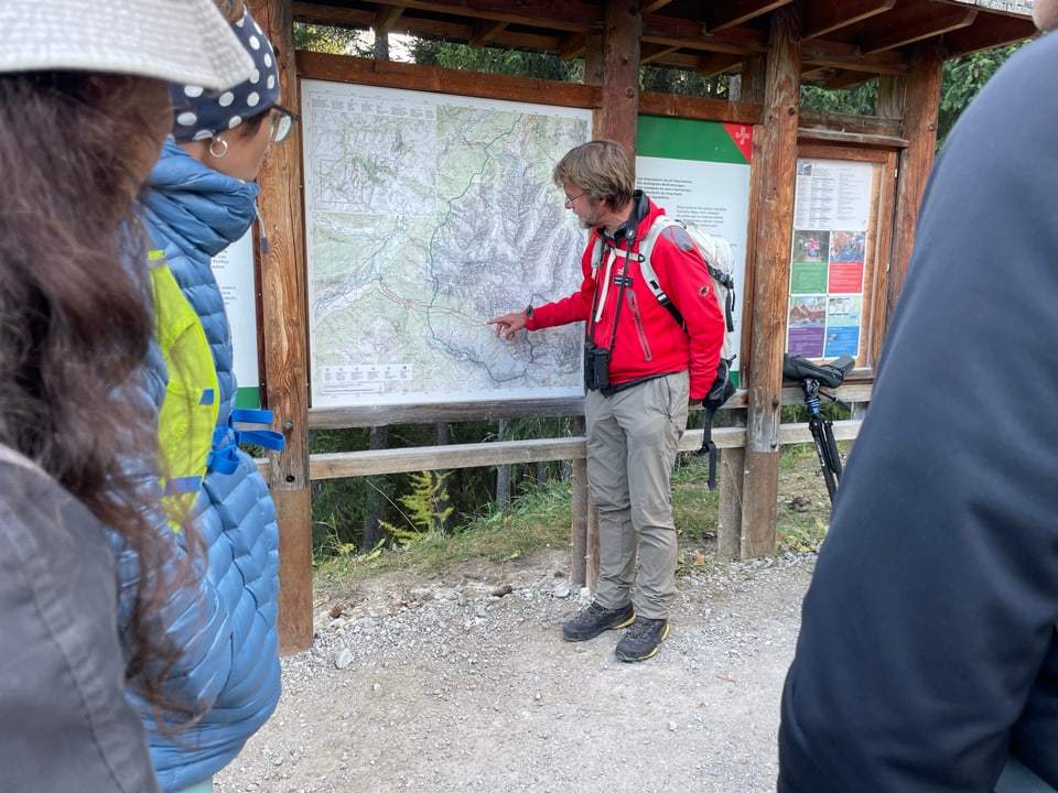 Wanderleiter erklärt der Gruppe ein Gebiet an einer Karte.