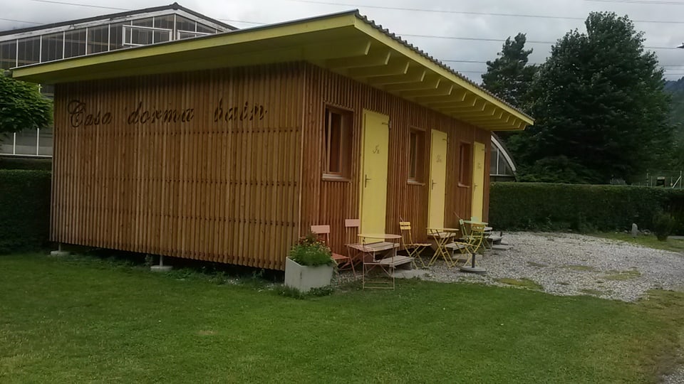 Ina casa da lain cun tetg e trais portas melnas cun inscripziun Casa dorma bain - ina chasa cun chombras ch'ins po prender a fit.