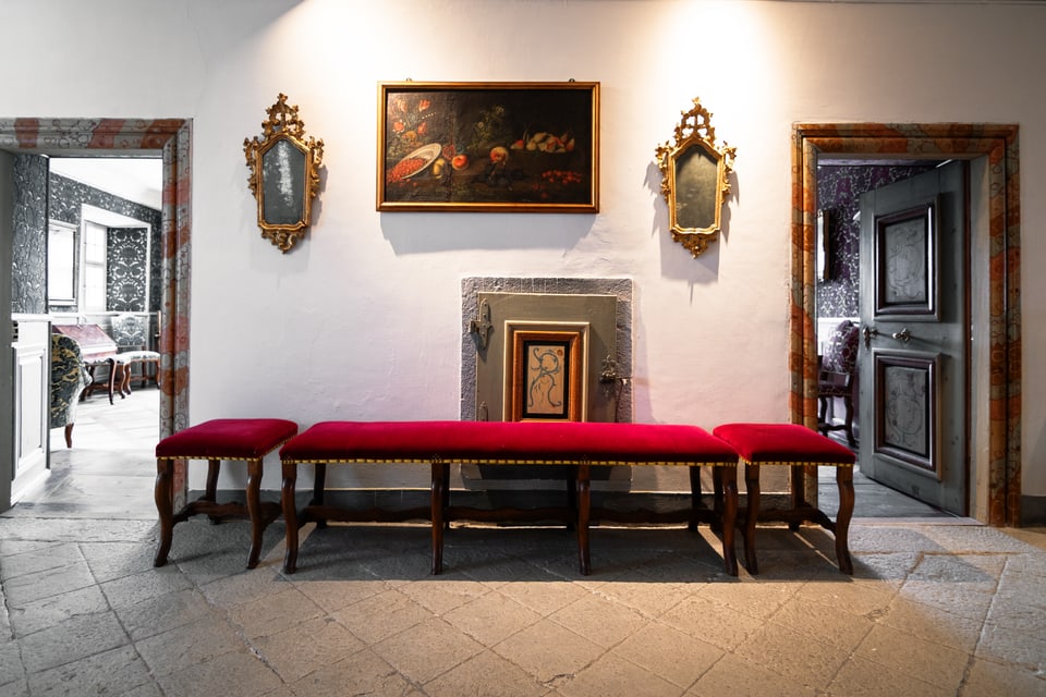 Im grossen Sulèr stehen rote Bänke vor einer Wand, an der alte Bilder hängen. Türen gehen davon ab.