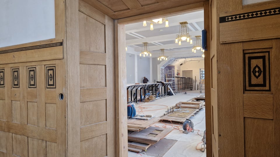 Sguard tras in porta tavlegiada en ina stanza gronda – ils funs zugliads cun folia, giu per terra material da fabrica..