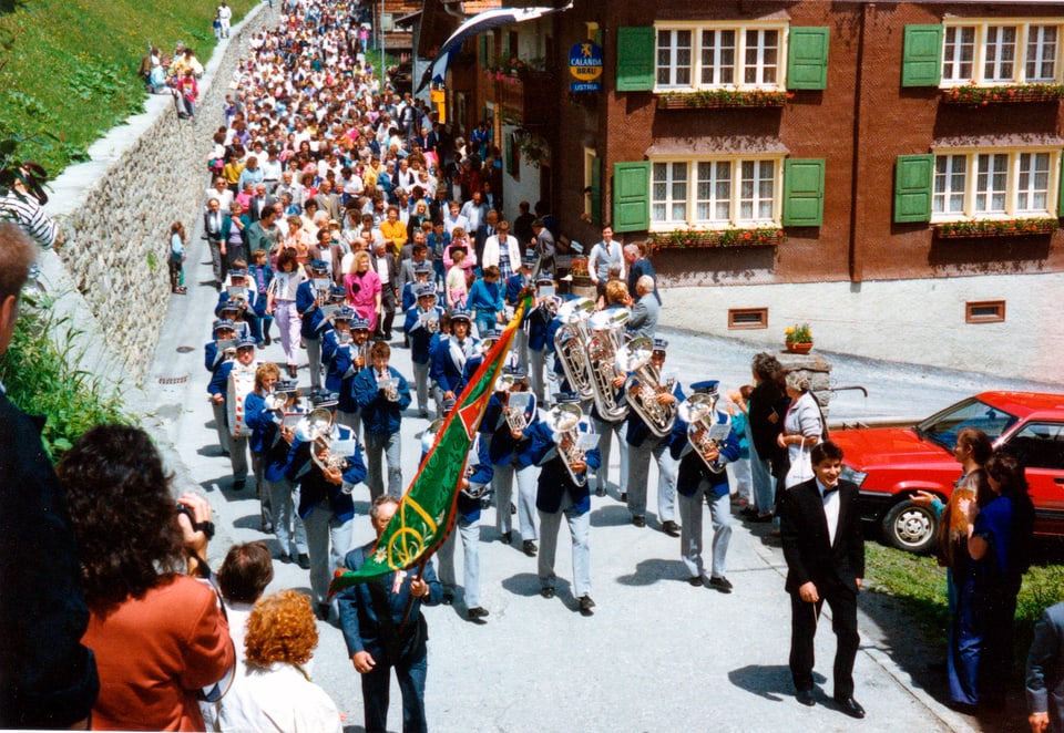 Grosser Umzug in Vrin, vorne marschiert die Musikgesellschaft in blauer Uniform.