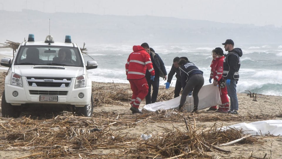 Mehrere Personen in Rettungskleidern an einem Strand.
