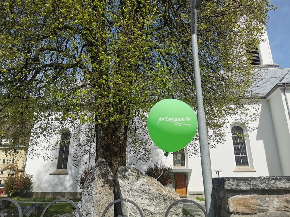 Ein grüner Ballon vor einem blühenden Baum. 