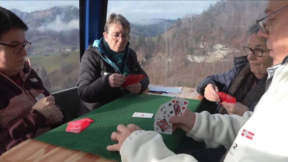 Quatter persunas giogan cartas en ina telecabina