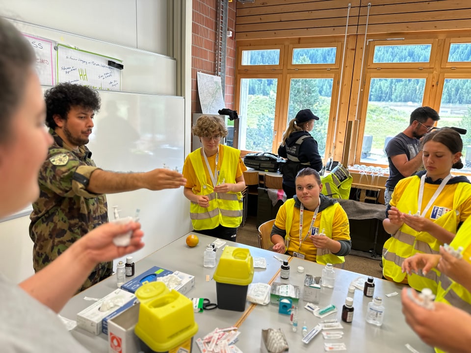 Demonstration wie eine Spritze funktioniert. Vier Schüler schauen einem Soldaten zu.