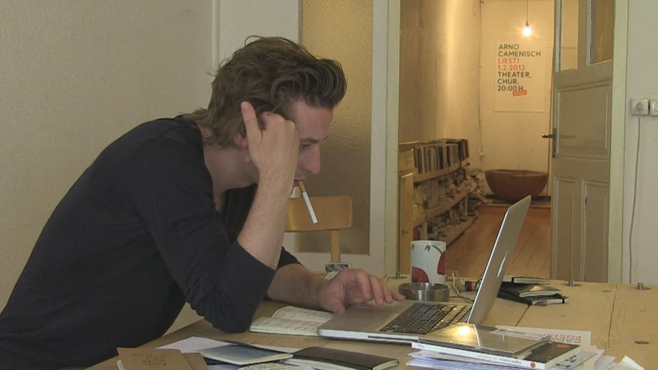 Arno Camenisch cun ina cigaretta en bucca avant il laptop vid scriver.