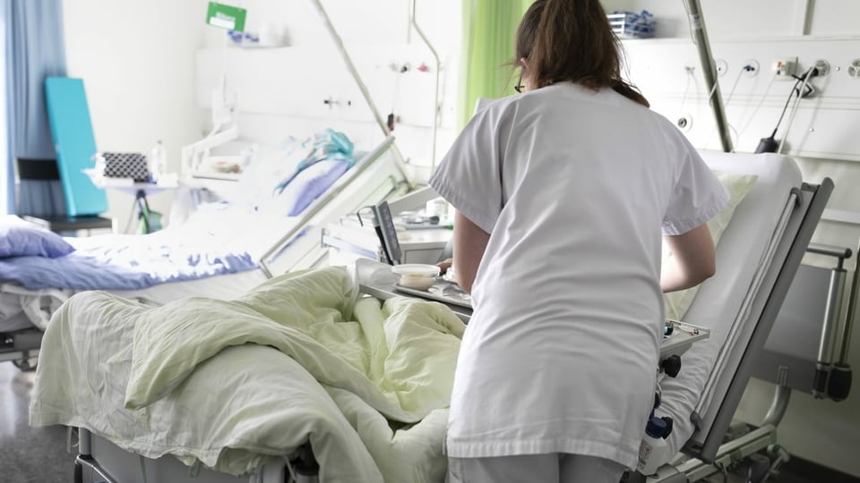 ina dunna che tgira ina persuna en in letg d'in ospital. 