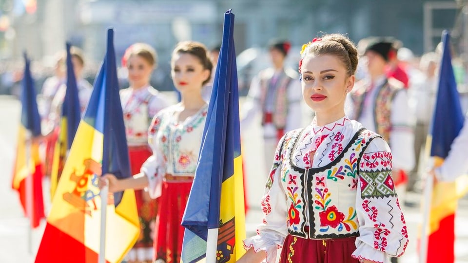dunnas giuvnas da la Moldavia tegnan en maun la bandiera naziunala