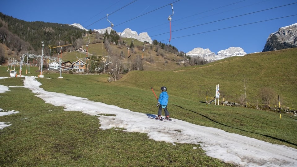 Kind fährt mit einem Skilift einer Kunstschneepiste hinauf.