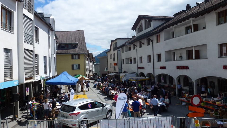 Plazza da festa cun bancs, maisas e blers visitaders.