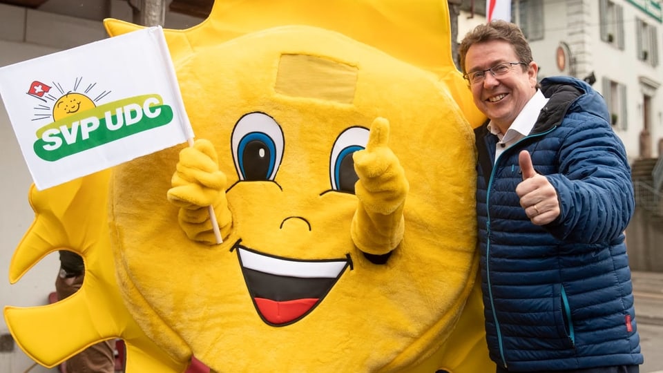 Il maletg mussa il president da la PPS Albert Rösti cun in sulegl sco mascot