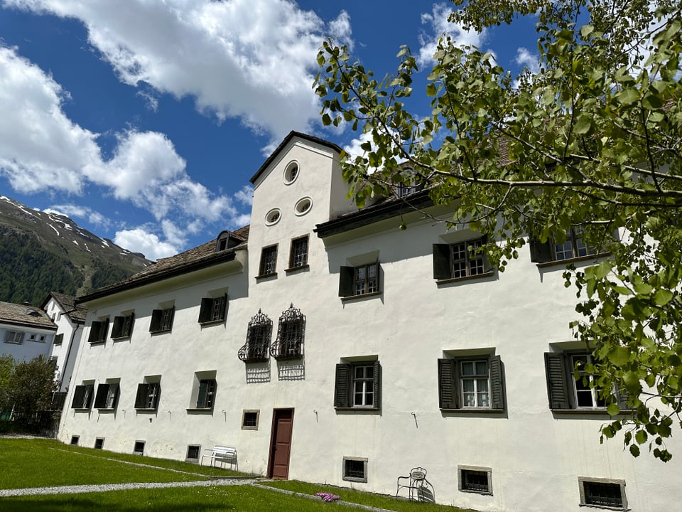Die Chesa Planta von hinten mit Garten. Ein grosses weisses Gebäude mit dunkelgrünen Fensterläden.