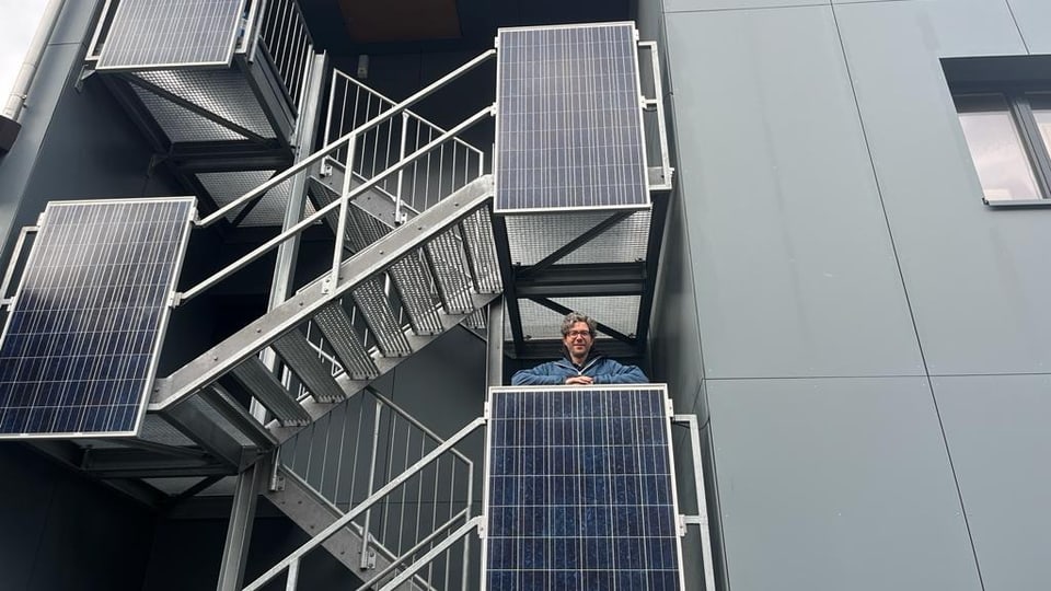 Herr Hassler, der auf dem Balkon seiner Firma steht, umgeben von Solarzellen