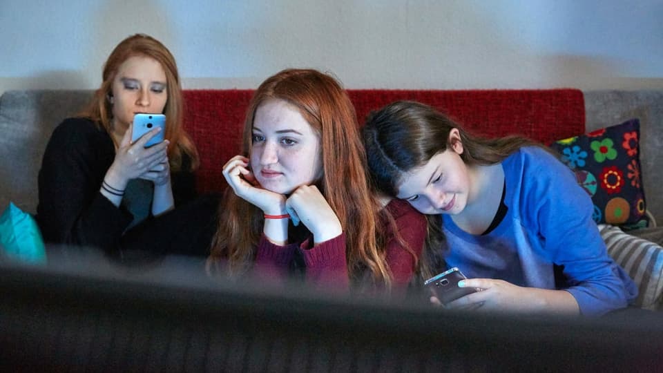 trais giuvenils avant la televisiun cun lur smartphones.