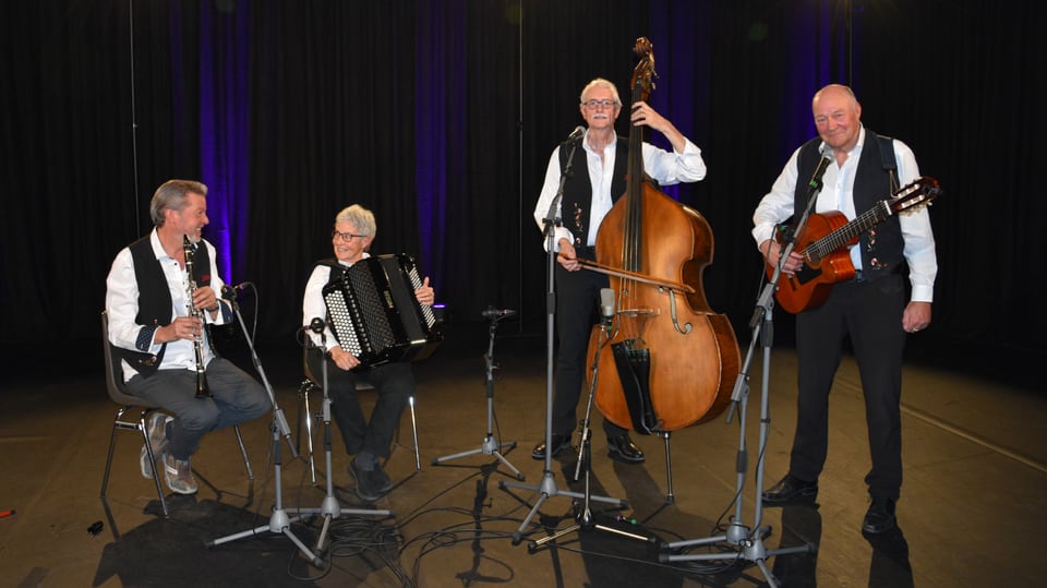 Vier Ländlermusikanten, Trio Jünaiver und Peder Rauch (Gitarre), alle mit schwarzen Hosen, schwarzer Weste und weissem Hemd resp. Bluse