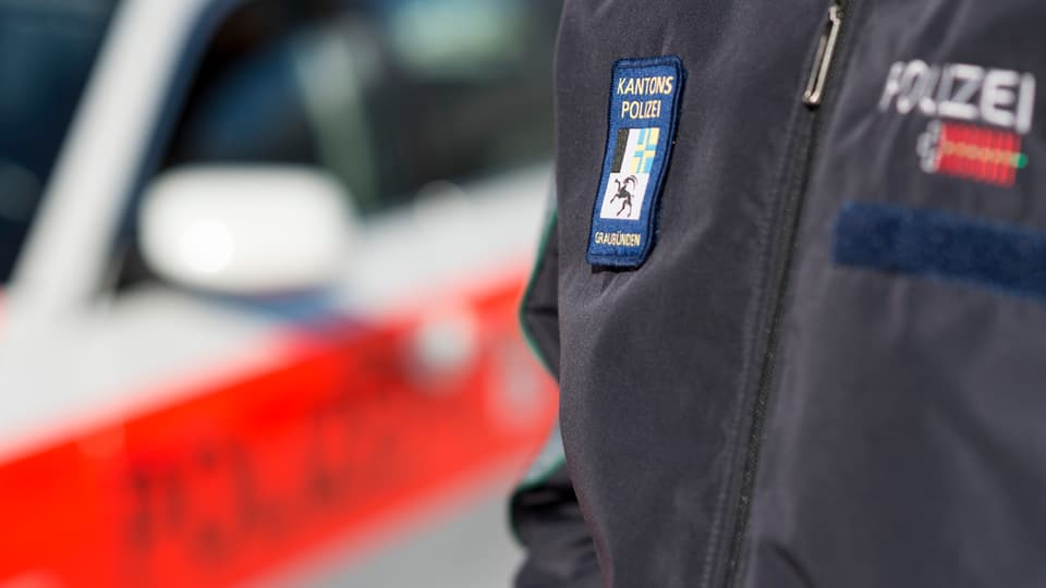 Policist da la polizia chantunala grischuna sper ses auto.