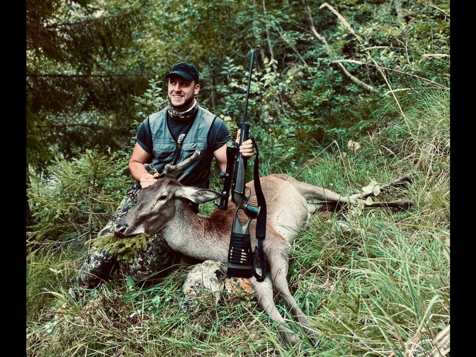 Jäger posiert mit geschossenem Hirsch im Wald, in der hand das Jagdgewehr.