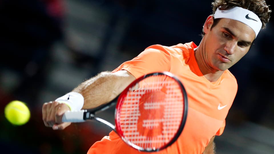 Roger Federer en in t-shirt oransch cun in rachet da tennis enta maun.