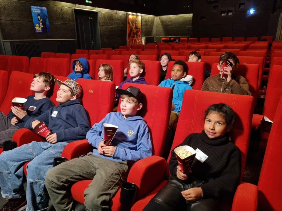 Kinder sitzen im Kino, mit Popcorn.