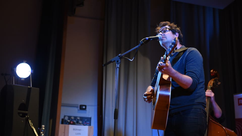 Curdin Nicolay e sia band In chantadur cun ghitarra sin il palc.