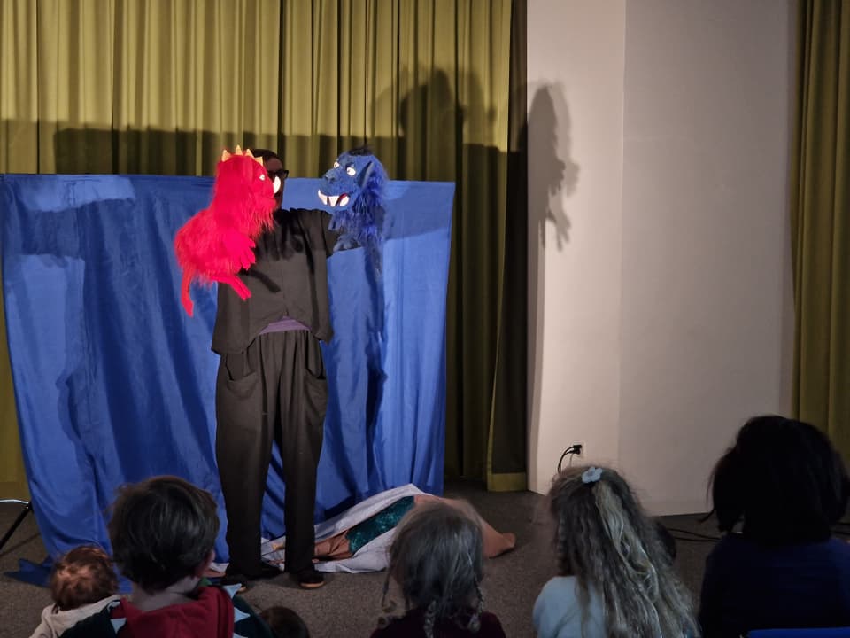 Eine Frau in schwarz hält zwei Handpuppen, ein rotes und ein blaues Monster.