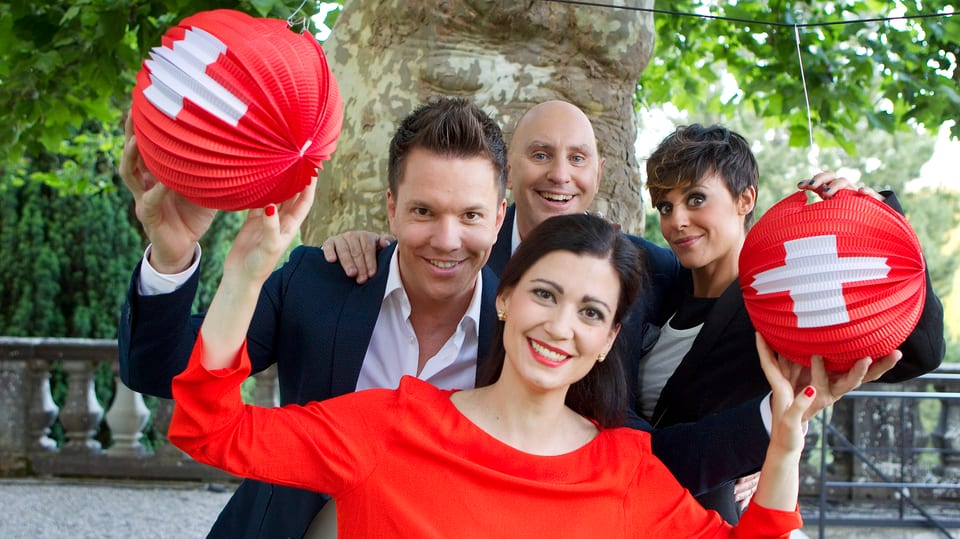 Sven Epiney (SRF), Maria Victoria Haas (RTR), Jean-Marc Richard (RTS) e Clarissa Tami (RSI) poseschan per ina foto sin ina terassa. Davontiers stat Maria Victoria Haas.