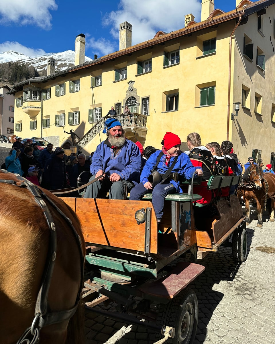Pferdekutsche mit Chalandamarz-Teilnehmern in blauen Hemden und roten Mützen